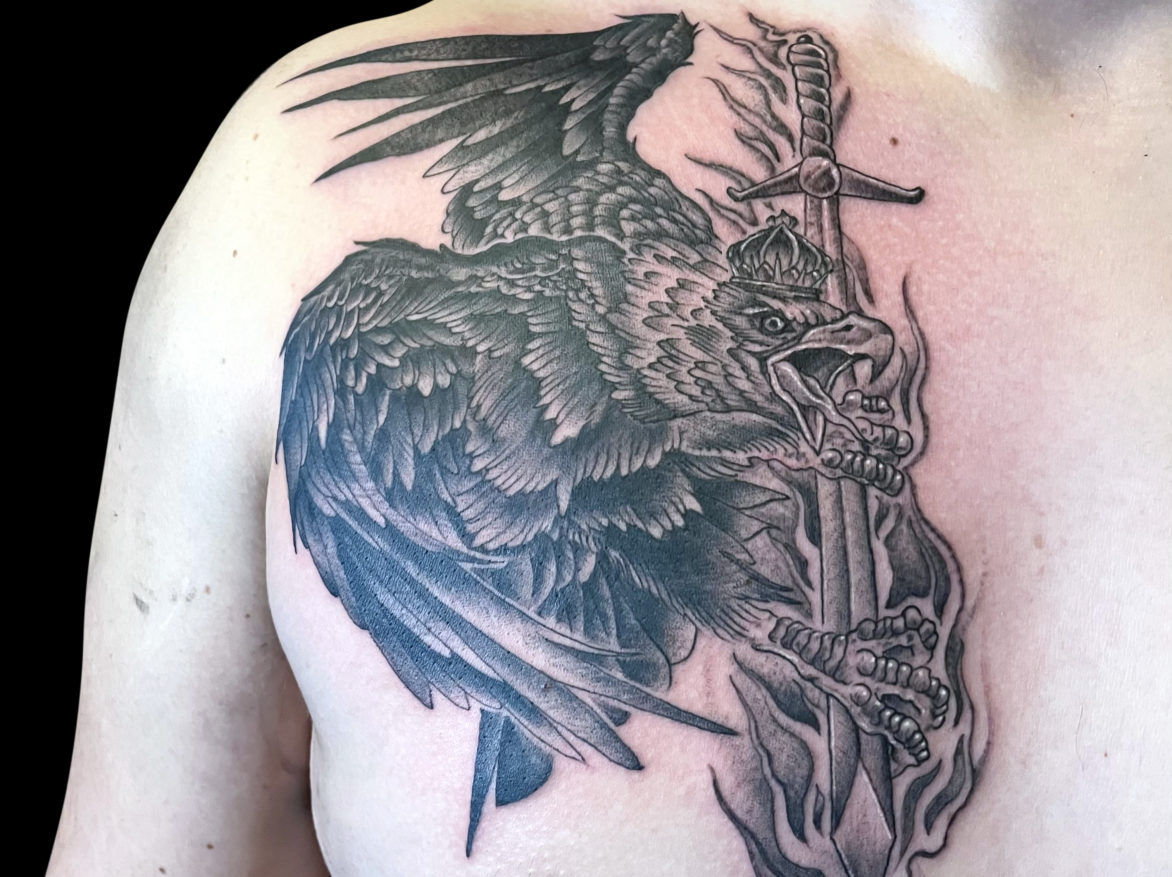black and grey tattoo of eagle holding flaming sword in its claws on chest