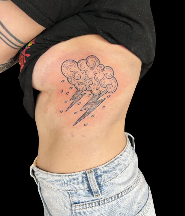 blackwork tattoo of illustrative cloud with two bolts of lightening coming out of the bottom and tiny rain drops tattooed on ribs