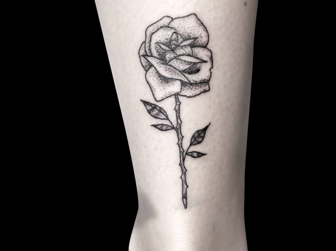 dotwork tattoo of a single rose with thorns shaded with dots on back of leg above ankle