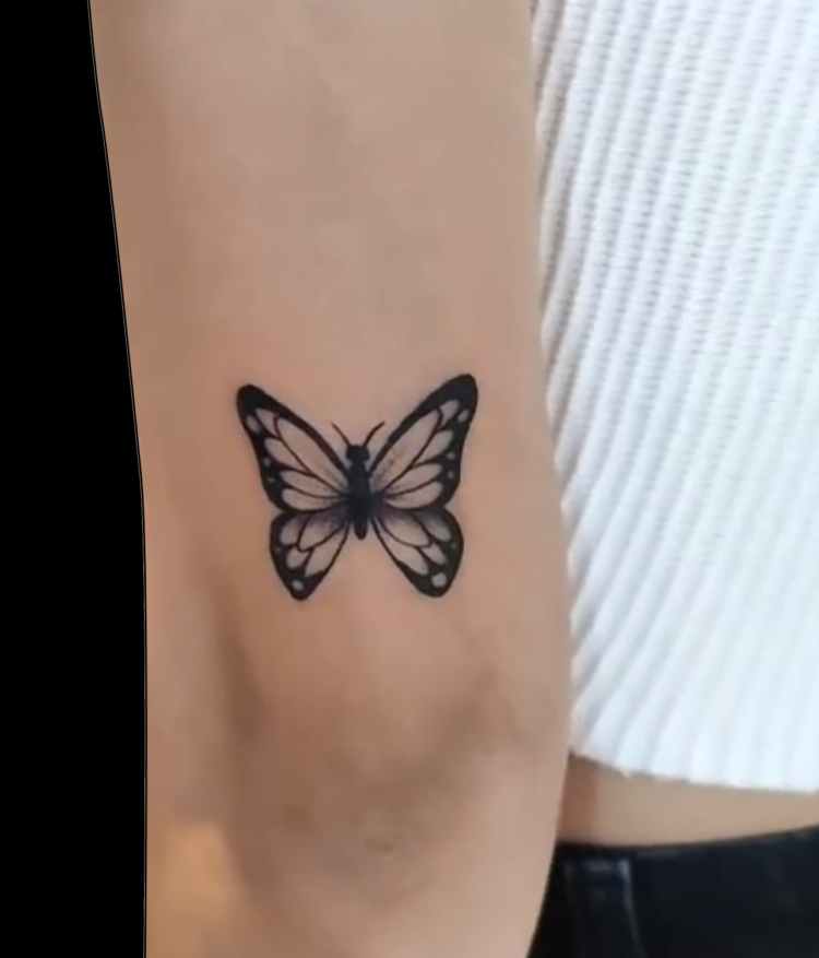 simple black butterfly tattoo with minimal shading tattooed on back of arm above elbow
