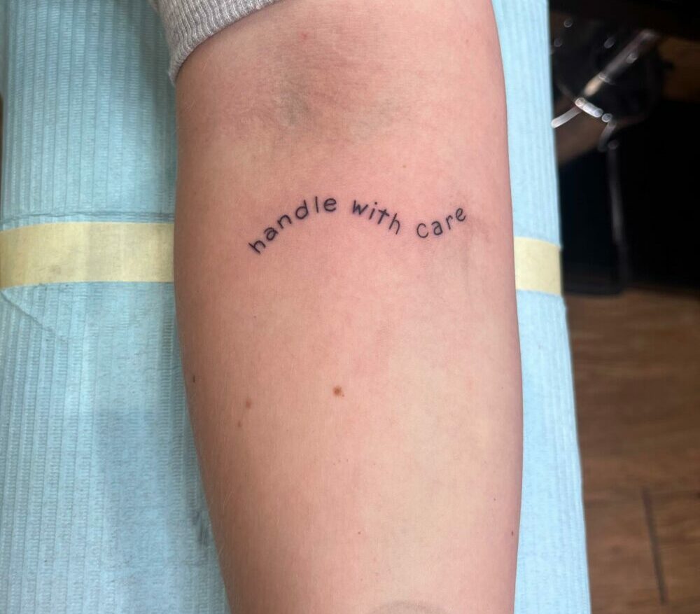 simple wavy text that reads: handle with care, tattooed on inner forearm